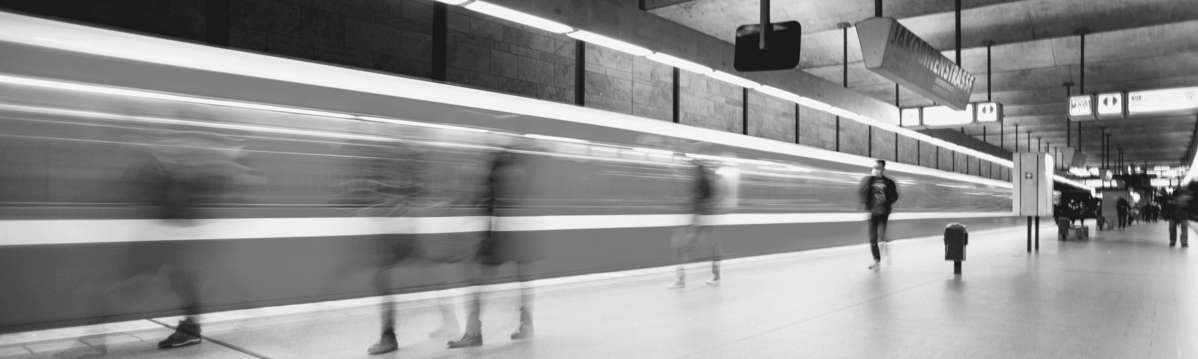 Gehende Personen am Bahnsteig, die in zeitlicher Bewegung dargestellt sind.