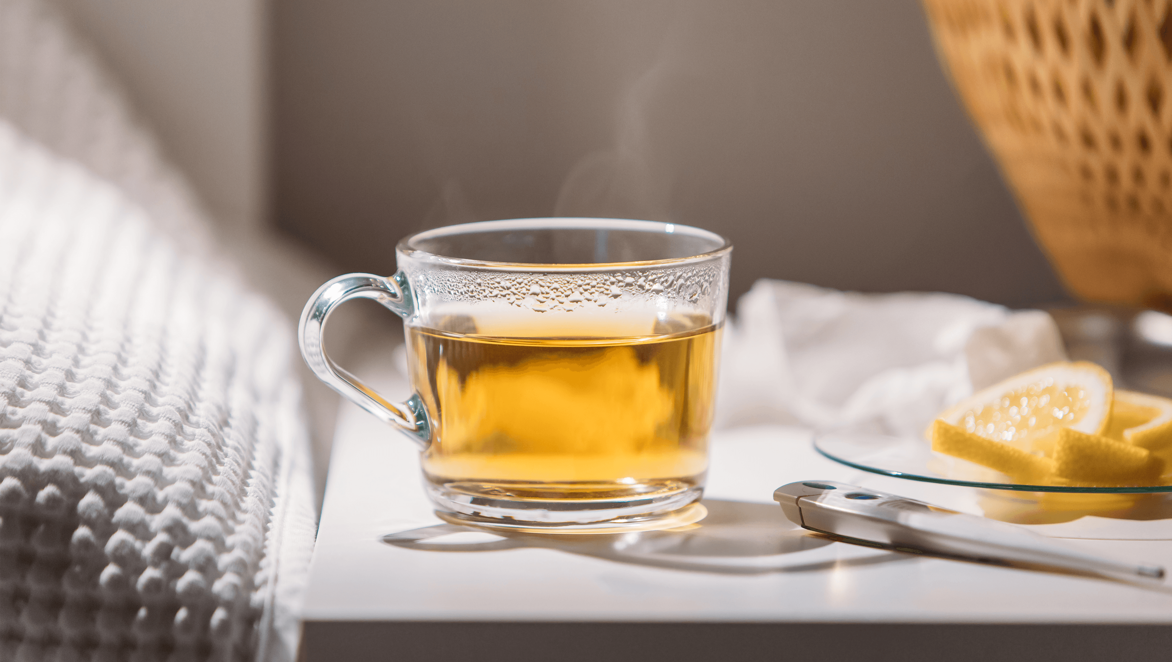 Headerbild zeigt eine Tasse mit Tee, ein Fieberthermometer und Zitronenscheiben, die auf einem Nachttisch liegen.  