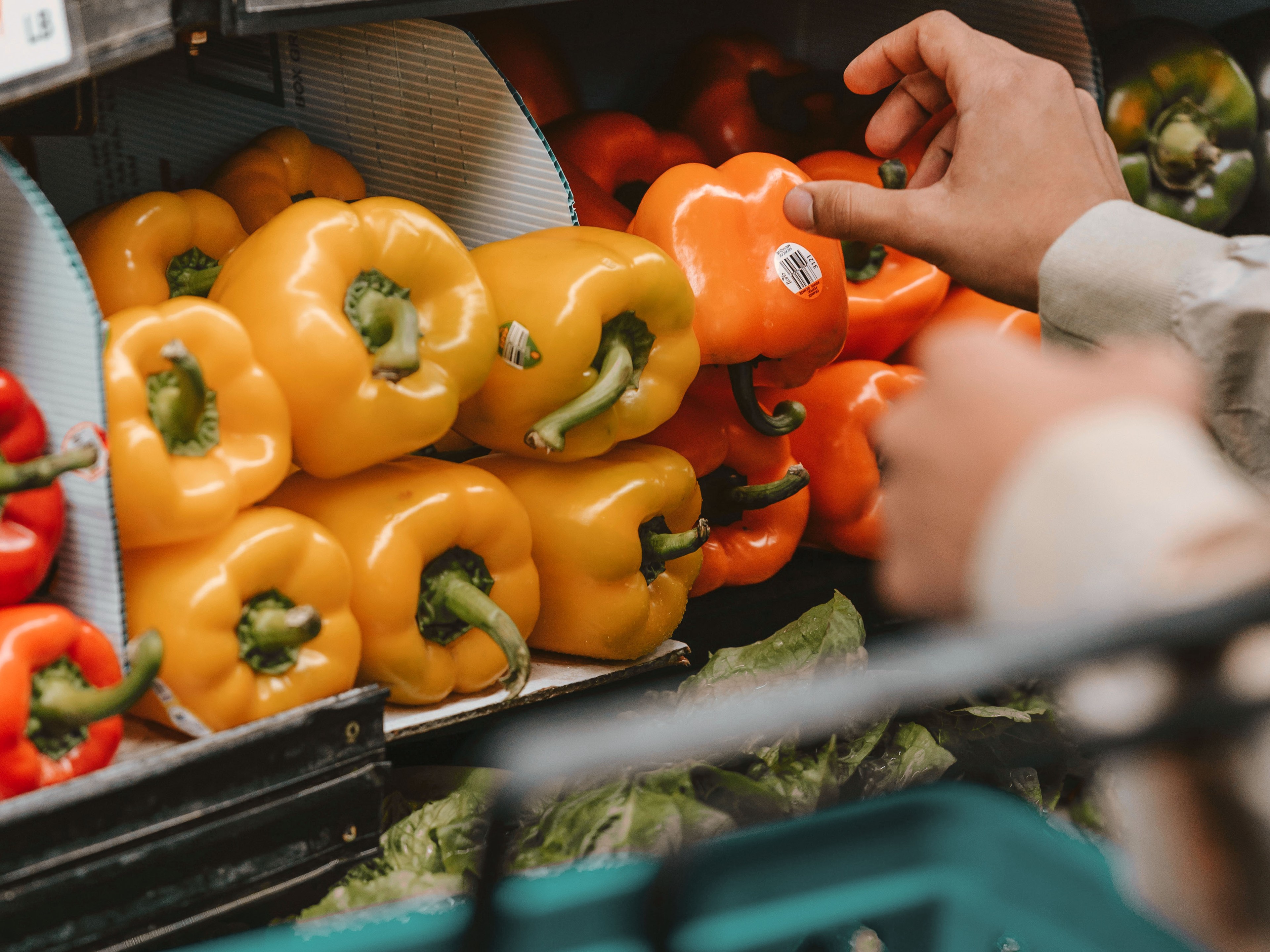 Person beim Einkaufen von Paprika im Supermarkt.