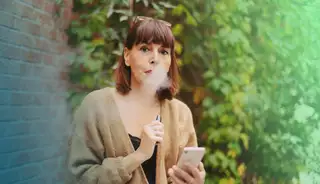 Headerbild zeigt Mitarbeiterin, die sich mit askDANTE am Smartphone zur Raucherpause in der Arbeitszeit ausstempelt.