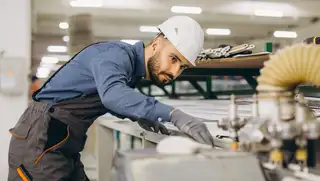 Headerbild zeigt einen Monteur, der eine Holzleiste in ein Metallgerüst schiebt und mit einem Akkordlohn vergütet wird.