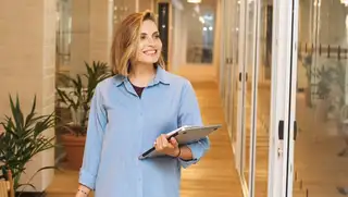 Headerbild zeigt Frau mit Laptop im Arm, die einen langen Flur im Büro entlangläuft und sich mit einem Transponder einstempeln möchte.