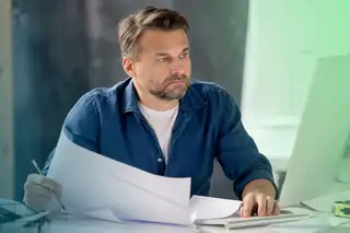 Headerbild zeigt Mitarbeiter am Monitor am Schreibtisch, der die Lohnabrechnung im Unternehmen prüft.