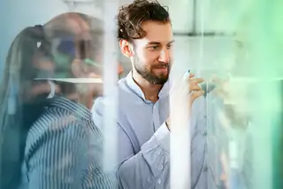 Headerbild zeigt zwei Mitarbeiter im Büro, die an einer Tafelwand zum Thema Resturlaub arbeiten und rechnen.