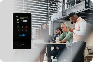 Business Terminal zur Zeiterfassung mit Mitarbeitern am Schreibtisch im Hintergrund